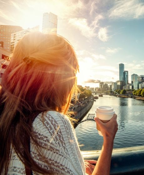 young woman drinking coffee on a bridge over a river in melbourne