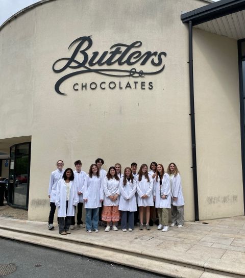 Students standing in front of the Butlers Chocolate sign, decked in their white warehouse coats.