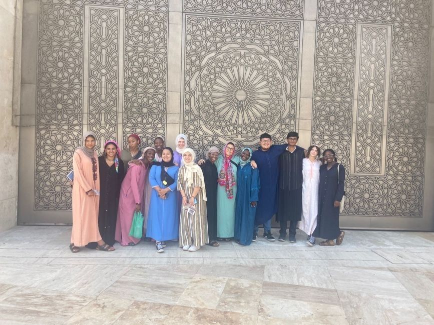 Students standing in front of a wall outside Hassan II Mosque with detailed plasterwork