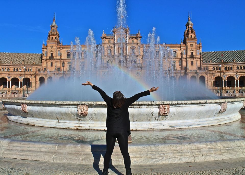 Student posing in front of fountain in Seville with a rainbow