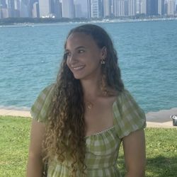 Profile picture of author, Emma Potts, standing in front of Lake Michigan in a green dress--looking off to the side