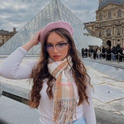 An art-obsessed girl in Paris standing outside of the Louvre wearing a pink beret with a matching scarf having the time of her life