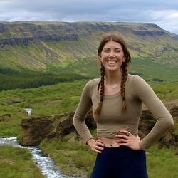 A photo of Megan on the top of a mountain in Iceland with a river and other mountains behind her.