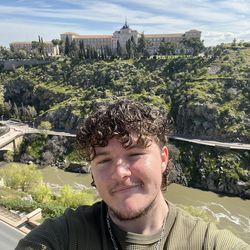 An image of myself posing over a river, with greenery and a castle in the background.