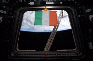 The Irish tricolour flag (green, white, orange) displayed in the window of the International Space Ship overlooking the Earth from Outer Space.