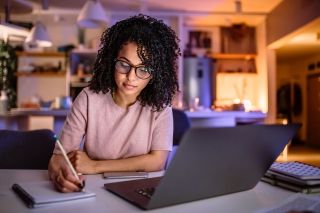 Woman taking notes with laptop open in front of her