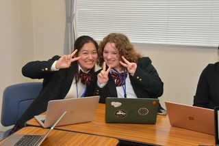 Two female high school students posing with their laptops in Japanese classroom
