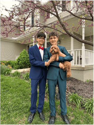 two male students dressed in formal suits holding a brown dog in front of a house - they are heading to prom