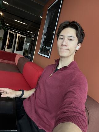 Person in a maroon sweater taking a selfie while seated on a red couch in a modern office lounge.