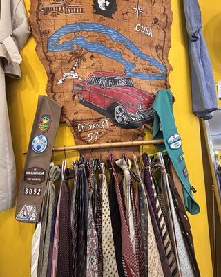 Clothes rack full off different neck ties. A girls scouts sash and a map of Cuba on the wall drawn in a western style.