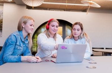 Three young women crowded around a laptop on a desk