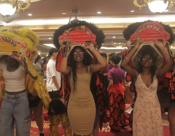 Three CIEE Global Navigator Students learn dragon dancing; they uphold two red and one yellow dragon heads. 