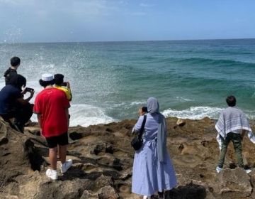 Students standing on a rock in front of crashing waves, looking out over the water