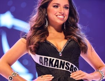 A young woman in a black dress with a sash that says "Arkansas" in front of a blue background