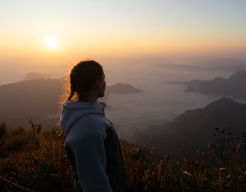 Girl looking out onto a view of fog and sunrise. 