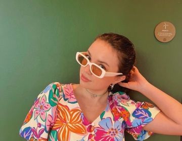 A girl in a colorful shirt and sunglasses against a green backdrop