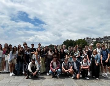 AM group posing for a photo on a bridge by the Seine, with the Eiffel Tower in the distance