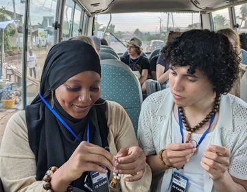 Max looks on as Monajah finishes her beading on the bus.