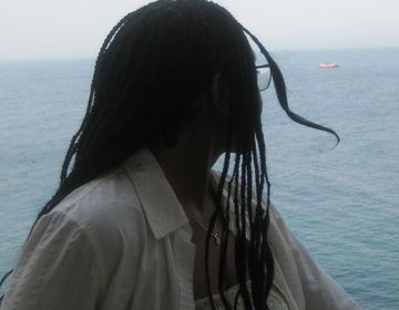 Image of Promise in Busan standing against a railing facing towards the backdrop of the sea