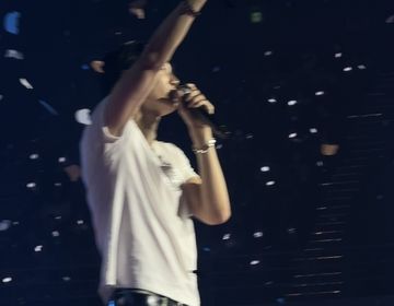 Kpop artist Kai is standing on stage waving to his fans as confetti falls around him