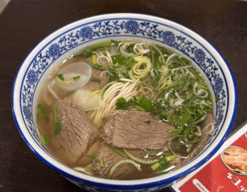 A bowl of warm pho with bean sprouts, cilantro, and beef.