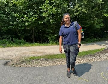 Maria M., a woman from Mexico and a CIEE-sponsored camp counselor, stands in front of the woods at Camp Sno-Mo in New Hampshire.