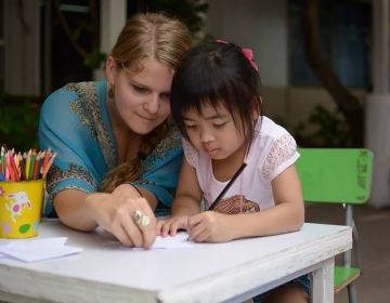 Teach Thailand teacher with student writing at desk