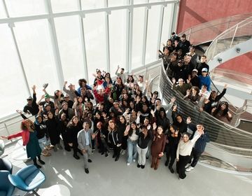 A group of 50 BMCC students and administrators standing in front of a spiral staircase and smiling up at the camera