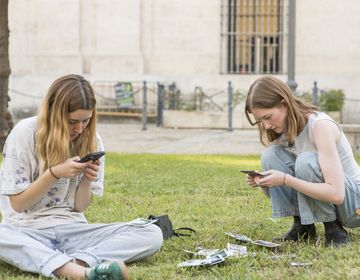 high schoolers on their phones outside in the grass