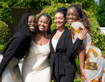 Four female students smiling cheek-to-cheek in front of a green, garden background