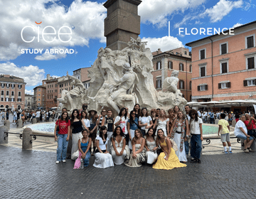 a group of 15 students standing in front of an old-looking water foundation in a town square in florence, italy