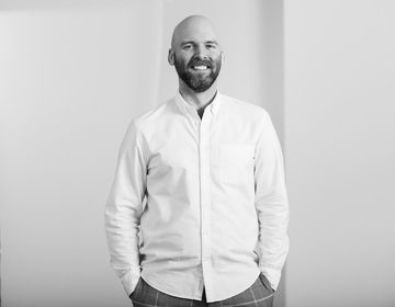 A man in a white button down shirt standing and smiling at the camera