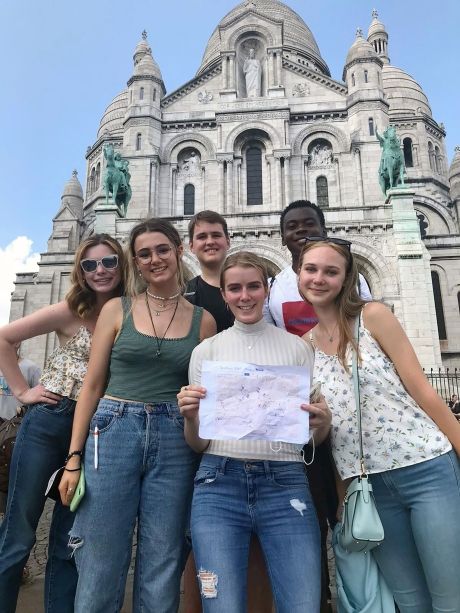 High school girls holding up paper in front of Montmartre in Paris
