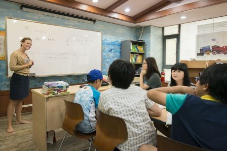Teacher in front of whiteboard smiling at class of students
