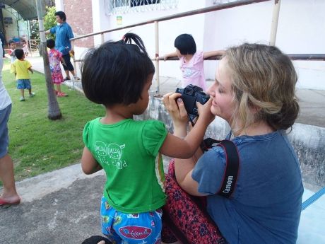 Young woman letting child inspect her camera in Thailand