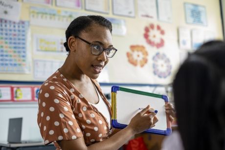 Teacher in classroom holding small whiteboard while teaching