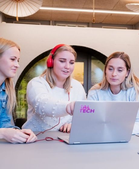 Three young women crowded around a laptop on a desk