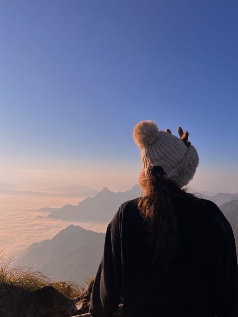 The back of a girl in a sweatshirt and beanie faces a sunrise over the mountains