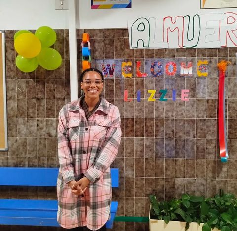 Lizzie standing in front of a "Welcome Lizzie" sign in the primary school