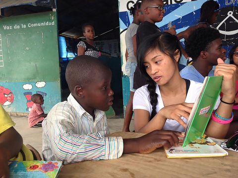 High school student abroad reading book to little boy