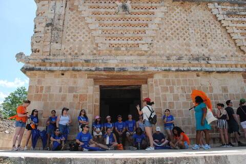 Students sit in the shade while their instructor teaches about the history of Uxmal