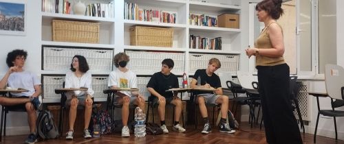 Teacher giving lecture to students sitting at desks against wall