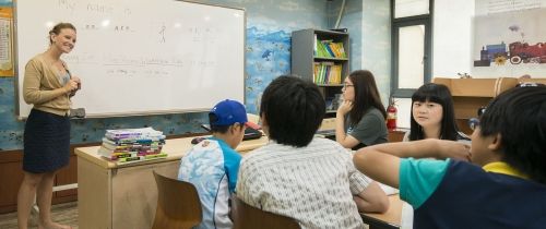 Teacher in front of whiteboard smiling at class of students