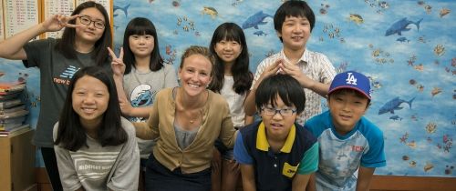 Teacher and students posing in front of ocean mural on wall of classroom