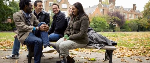 Adults sitting on a bench outside a building during the fall