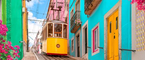 a yellow tram car going downhill in lisbon