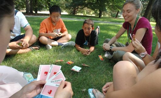 Counselors and kids playing a card game on the grass
