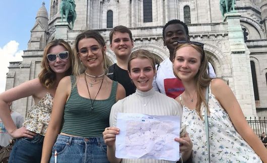 High school girls holding up paper in front of Montmartre in Paris