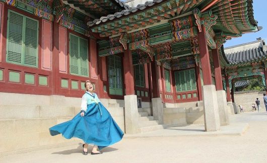 Teacher in traditional Korea dress smiling in front of a temple