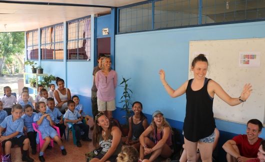 Young woman gesturing in front of group of children outside